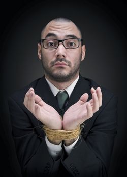 A man on a suit shows his tied hands with a puzzled expression. 