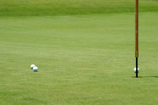 Three golf balls near the flagstick on the green.