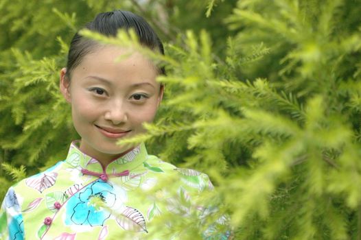 Chinese girl in park, hidding behind green bushes.