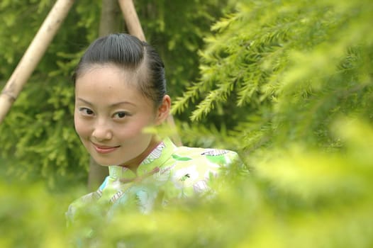 Chinese girl in park, standing behind green bushes.