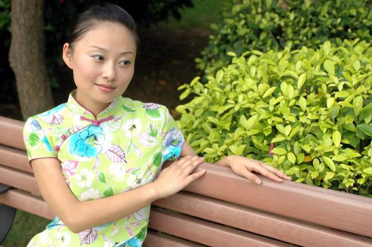 Chinese girl in park, sitting on bank, relaxing.