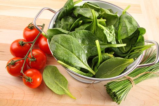 Strainer with fresh spinach leaves and tomatoes