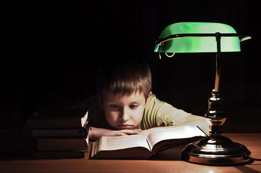 boy reads book in dark room under green lamp