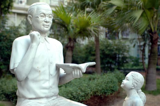 Sculpture made of stone - showing Chinese teacher, holding book and giving lessons to young girl.