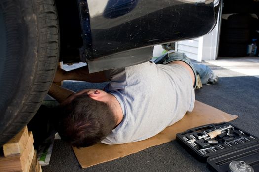 A young man laying underneath a car doing repairs or maintenance on the vehicle.