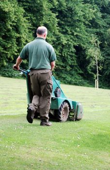 A photograph of a man mowing the grass in a public park