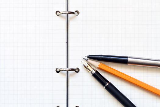 Two pens and wooden pencil lying on open spiral notebook