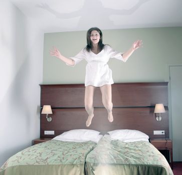 happy young girl jumping on bed in hotel room, selective focus on face, hands and legs motion blurred