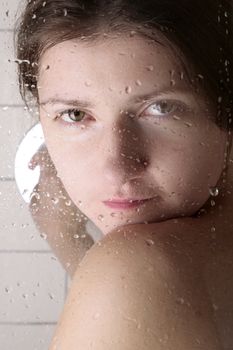 young woman looking through the cabin shower glass with water drops on it