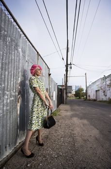 Woman with pink hair wearing polka dot dress in alley with purse