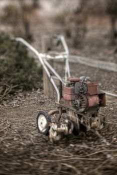 A classic rototiller, sitting by a split rail fence.