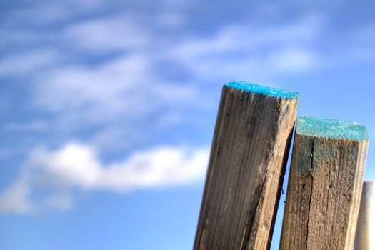 A couple of posts leaning against a fence, with a blue sky in the background.