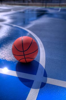 A basketball sitting nead the line on a blue outdoor basketball court