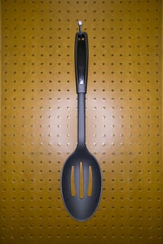 Slotted cooking spoon on a pegboard hook