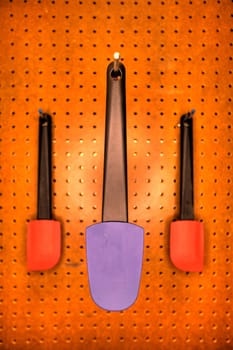 Professional cooking utensils in a restaurant kitchen, hanging o a pegboard wall.