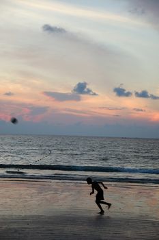 Boy playing football on beach. The player and ball is in motion.