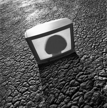 CRT monitor on a dry lakebed with silhouette of a person on the screen.