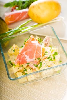 fresh home made parma ham and potato salad,with raw ingredients around with bowls and dishware on a table