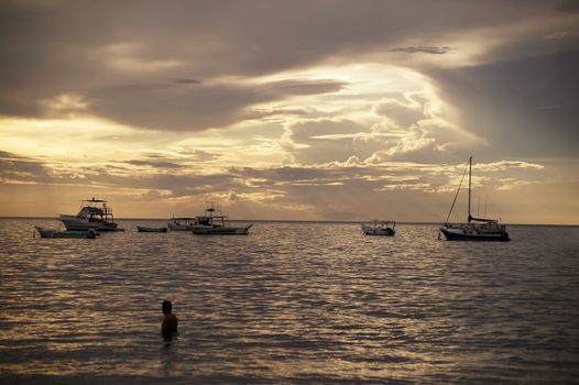 Costa Rica sunset with Boats and single bather in the Pacific Ocean