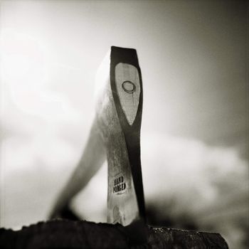 Hand Forged Ax embedded in log, under a cloudy sky.