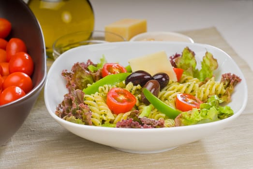 fresh healthy homemade italian fusilli pasta salad with parmesan cheese,pachino cherry tomatoes, black olives and mix vegetables ,dressed with extra-virgin olive oil and pesto sauce