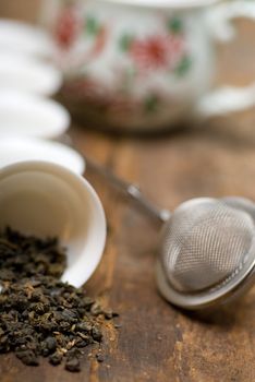 dry green chinese tea set,with strainer closeup,cups and teapot on background over old wood board