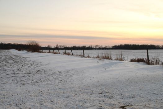 A snowy field with a fence set against the evening sky