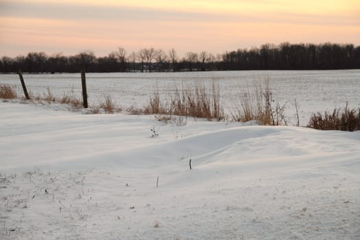 A snowy field with a fence set against the evening sky