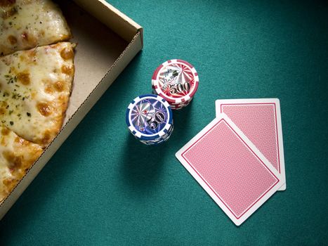 Two cards, two piles of chips and a box of pizza over a green felt.