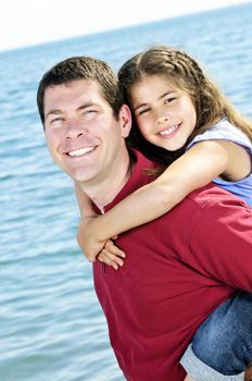 Portrait of father giving piggyback ride to daughter at seashore