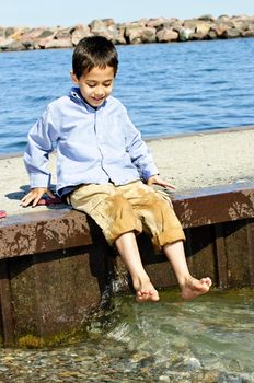 Portrait of young boy dipping feet in lake from pier