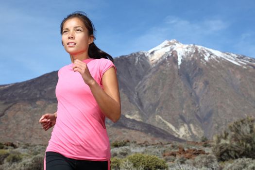 Sporty woman running on trail on mountain / volcano Teide on Tenerife. Beautiful mixed chinese asian / caucasian female model.