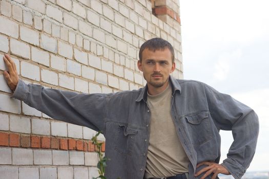 young man in a jeans jacket on a background of a brick wall