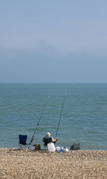 A man sea fishing on a pebble beach