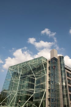 A glass office building in london with a coludy blue sky