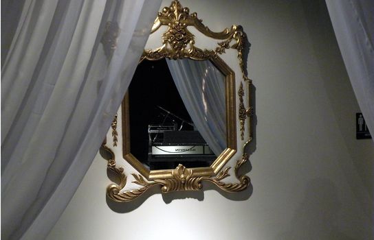 a mirror with the reflection of a piano, alone in the background