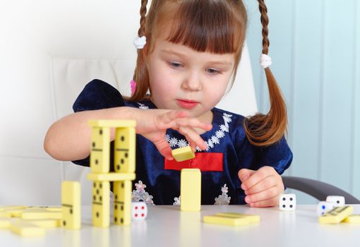 A child playing with dominoes sitting at the table