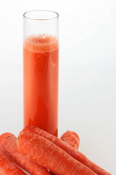 Carrot juice in a high glass and some carrots in the foreground.