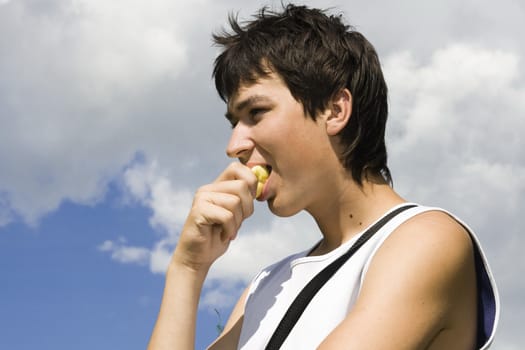 Young male eats apple with blue sky at background