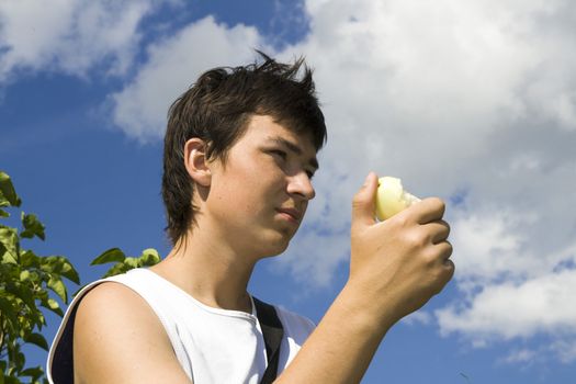 Young male eats apple with blue sky at background