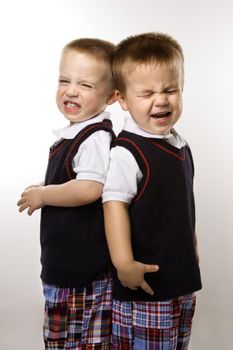 Caucasian twin boys crying standing against white background.