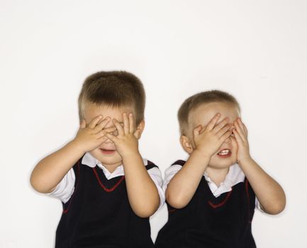 Caucasian male children twins with hands over eyes.