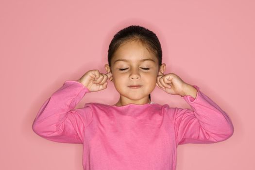 Female Hispanic girl with fingers in ears and eyes closed.