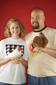 Caucasian mid-adult man and woman holding chickens.