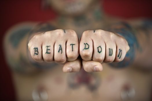 Caucasian mid-adult man with tattoos and piercings holding out fists reading beat down.