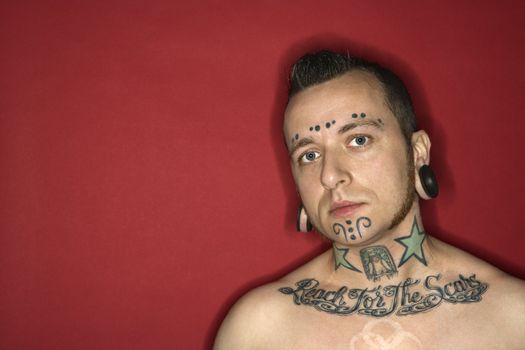 Caucasian mid-adult man with tattoos and piercings.