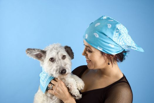 Hispanic mid-adult woman holding small white dog wearing matching bandanas.