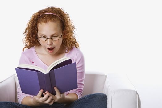 Caucasian female child sitting reading book looking surprised.