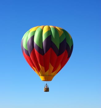 A multi colored Hot Ait Ballon rises into a clear bright sky