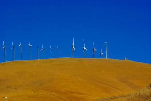 Wind powered  electric generating stations stie on top of  dry grass covered hill in Livermore California.